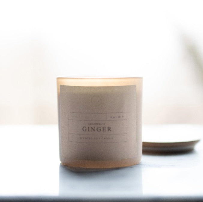 Candle labeled 'Ginger' on a white surface with a blurred background
