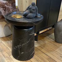 Black marble side table with a sculpture and candle on a wooden floor.