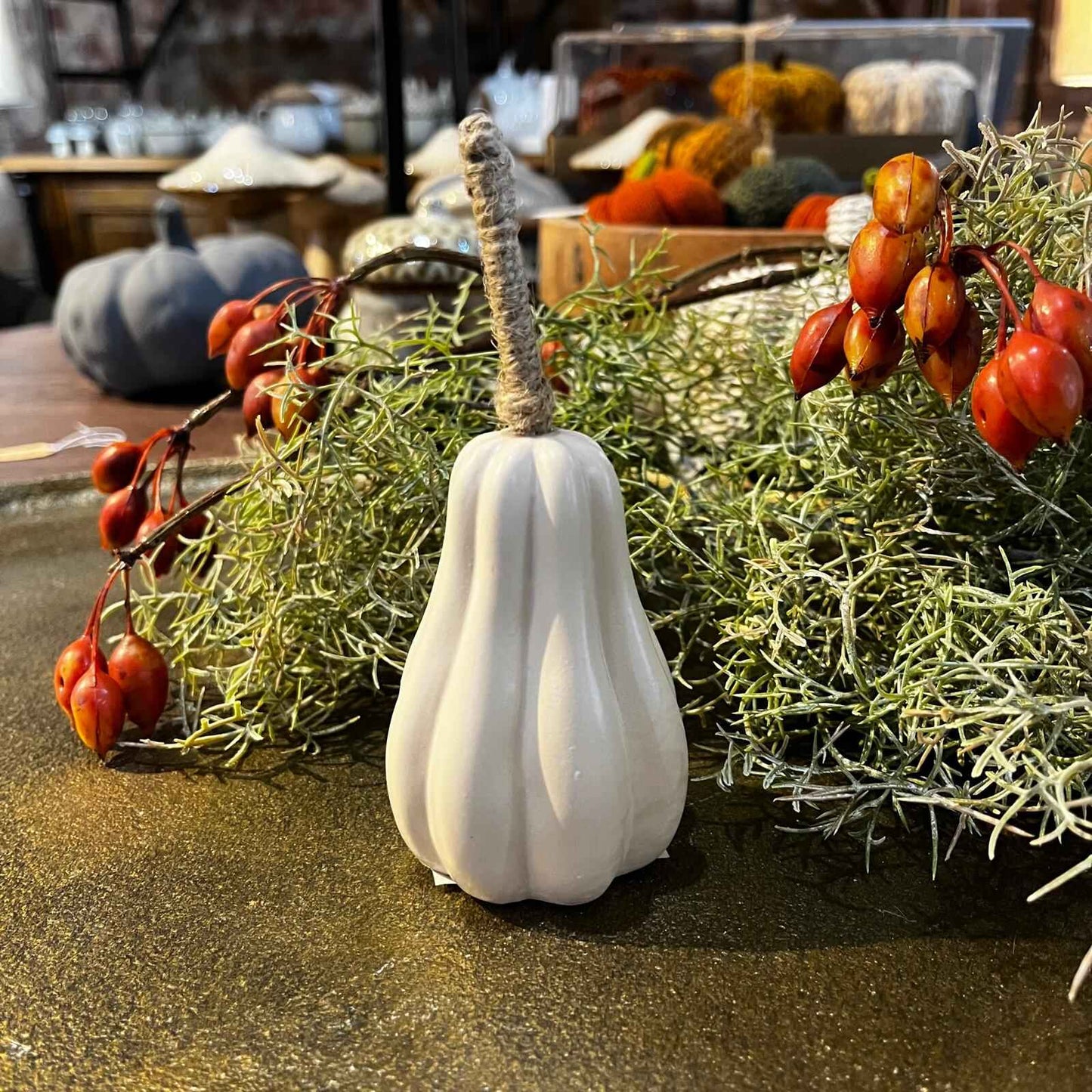 White decorative pumpkin with greenery and red berries on a table