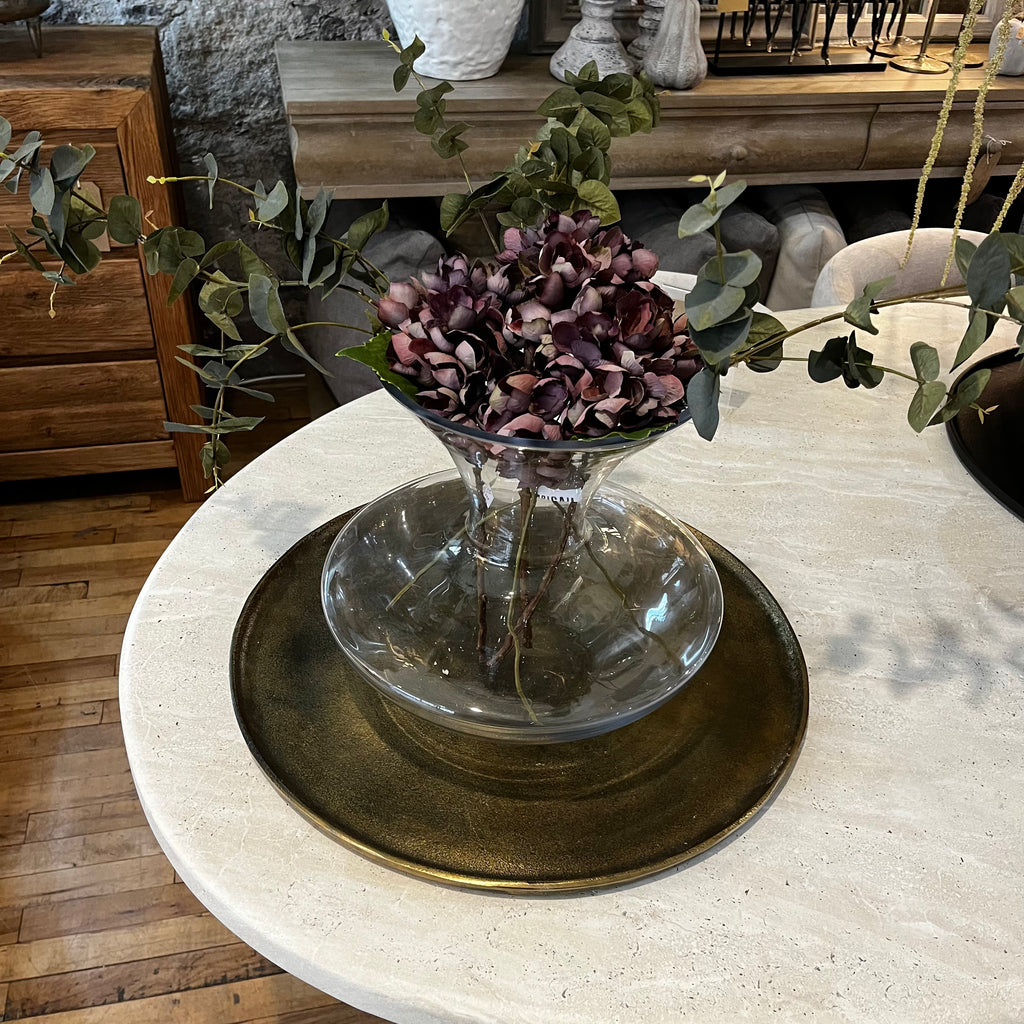 Clear glass bowl with purple flowers on a round table with decorative elements.