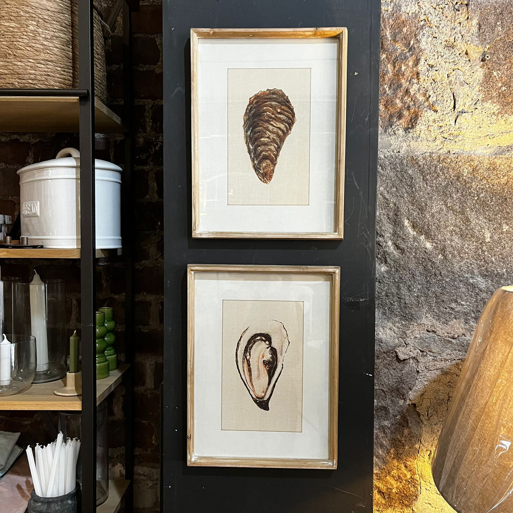 Two framed illustrations of oysters on a wall next to a rustic stone wall.