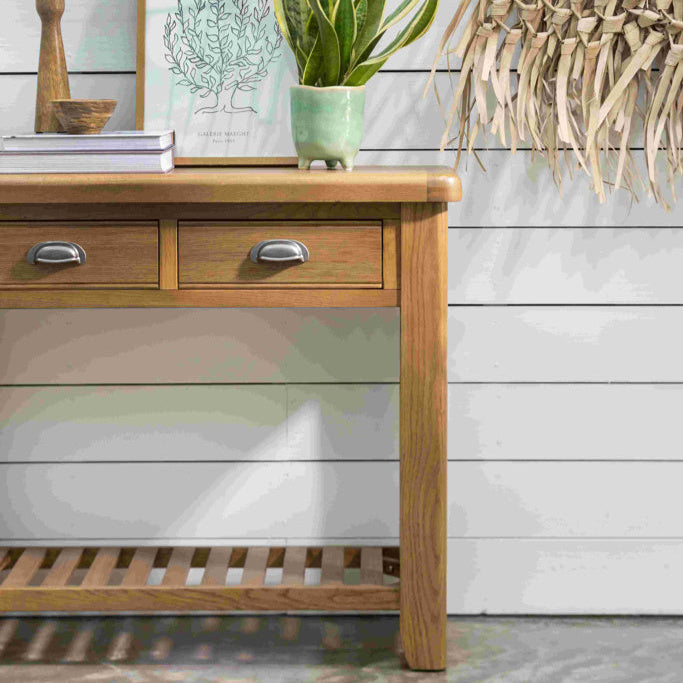 Wooden side table with a plant, framed picture, and candle on a light wooden floor.