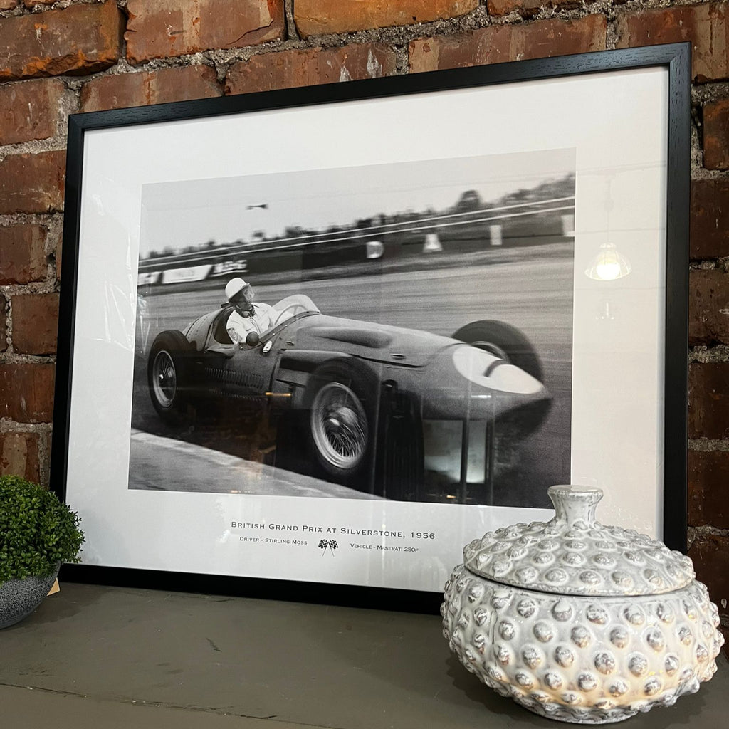 Framed black and white photograph of a racing car on a brick wall background
