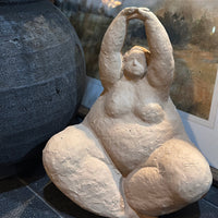 Stone sculpture of a seated figure with arms raised next to a large stone vase.