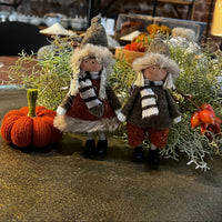 Two small dolls in winter clothing with a knitted pumpkin and greenery on a table.