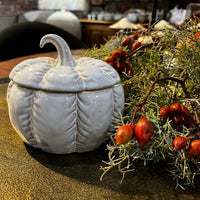 White ceramic pumpkin-shaped container on a table with decorative elements