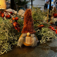 Decorative gnome with plaid outfit and red hat among greenery and berries.