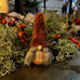 Decorative gnome with plaid outfit and red hat among greenery and berries.