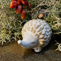 Decorative hedgehog figurine on a textured surface with greenery and berries in the background