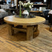 Round wooden coffee table in a store setting with various decor items.
