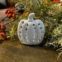 Decorative ceramic pumpkin with cut-out patterns on a surface with greenery and berries.