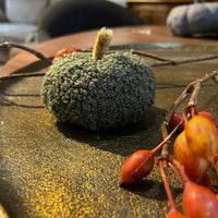 Decorative pumpkin with foliage on a textured surface with berries and branches.