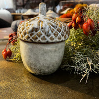 Decorative acorn with textured surface on a wooden surface with foliage and berries.