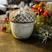 Decorative acorn with textured surface on a wooden surface with foliage and berries.