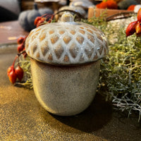 Decorative ceramic acorn with textured lid on a surface with autumn elements.