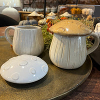 Two ceramic mugs with mushroom-shaped lids on a wooden surface.