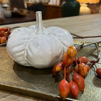 White ceramic pumpkin decoration on a reflective surface with blurred indoor setting
