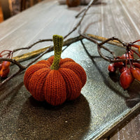 Knitted pumpkin decoration on a wooden surface with branches and berries.