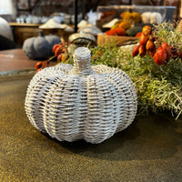 Decorative woven pumpkin on a table with autumn decorations in the background