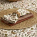 Decorative table setting with woven placemats and patterned napkins on a matching tablecloth.