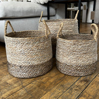 Three woven baskets on a wooden floor with a neutral background