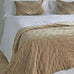 Beige quilt on a bed with white bedding and pillows.
